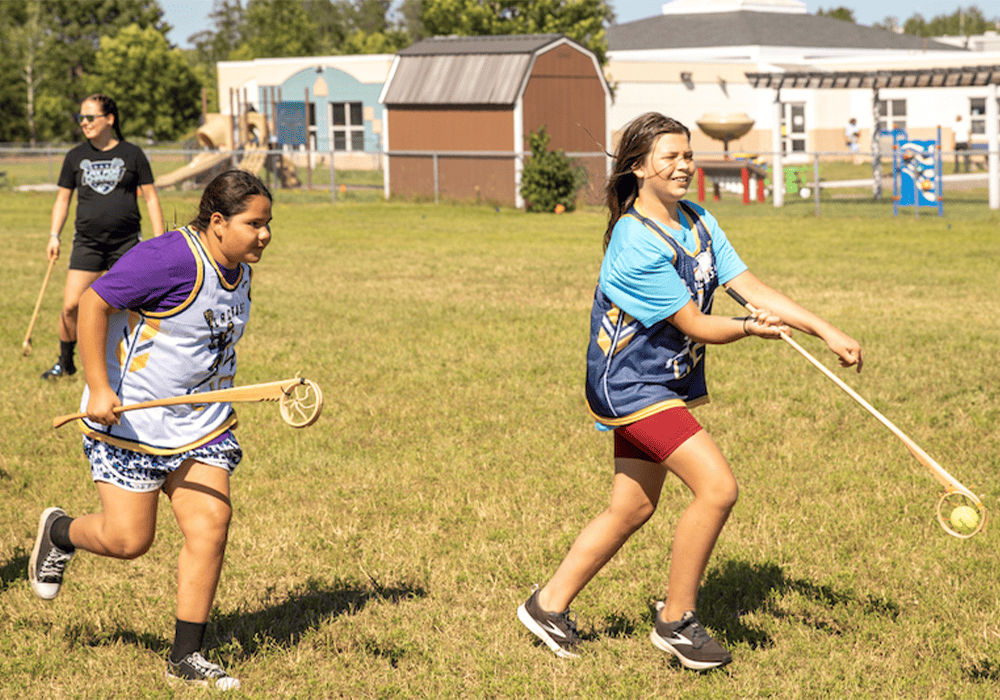 Two Indigenous young people are playing lacrosse on a field.