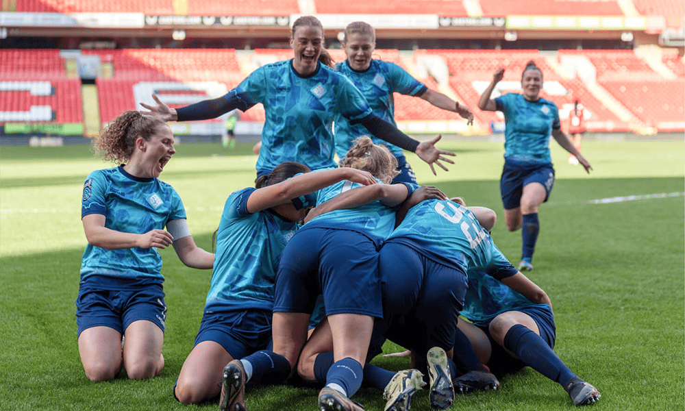 A group of football players from London City Lionesses in blue uniforms celebrating a goal with joy and excitement on the pitch.